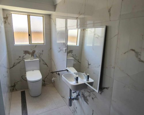 A bathroom with a toilet, sink and mirror.